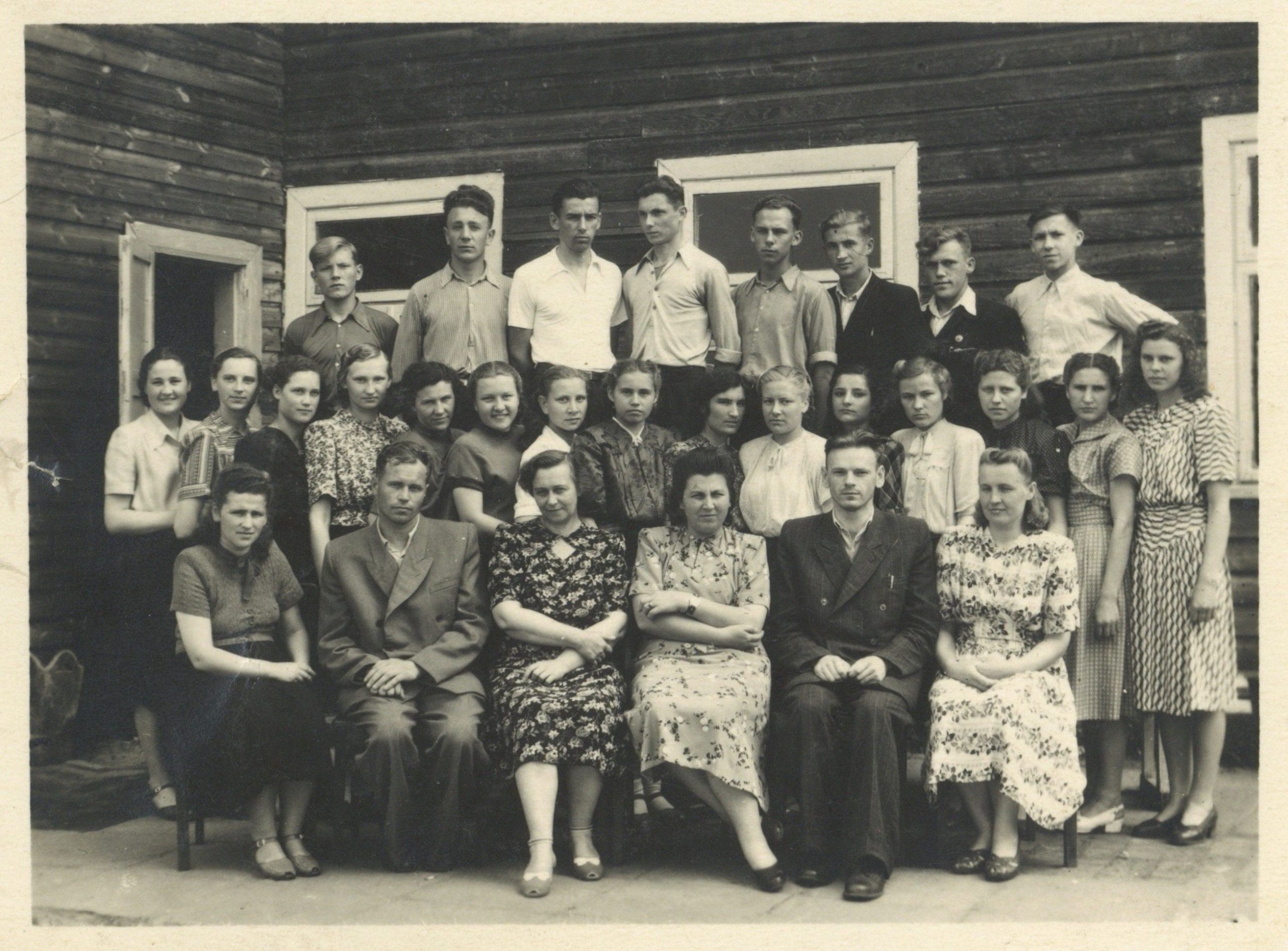 L. K. Ulevičius (stovi trečioje eilėje antras iš dešinės) su klasiokais ir mokytojais prie mokyklos pastato. 1955 m. Fotografija iš Lietuvos švietimo muziejaus rinkinių.