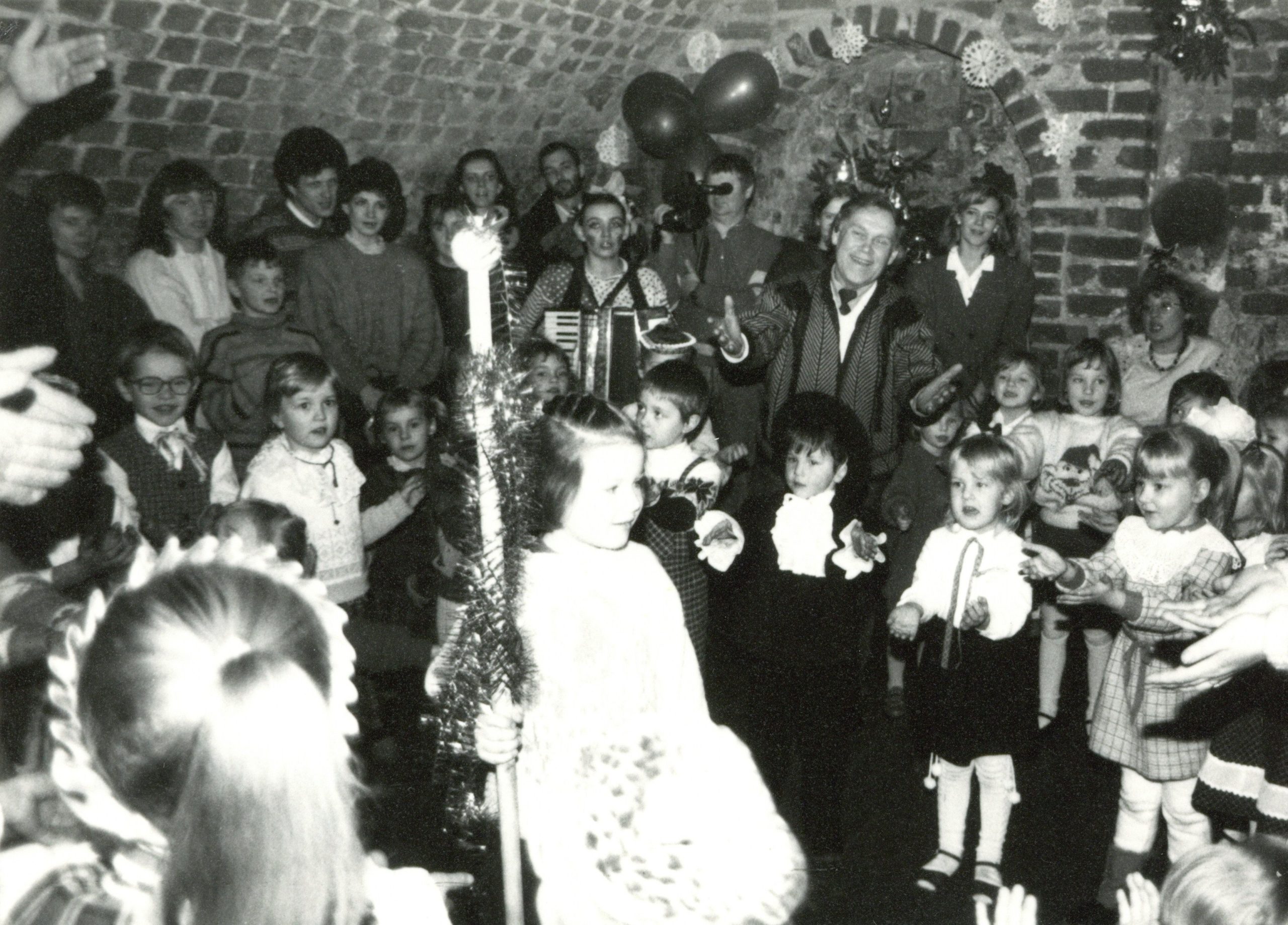 Tautinės muzikos ansamblio „Tututis“ vokalo vadovas L. K. Ulevičius su jaunaisiais atlikėjais šventinėje Naujametinėje programoje. 1991 m. Fotografija iš Lietuvos švietimo muziejaus rinkinių.